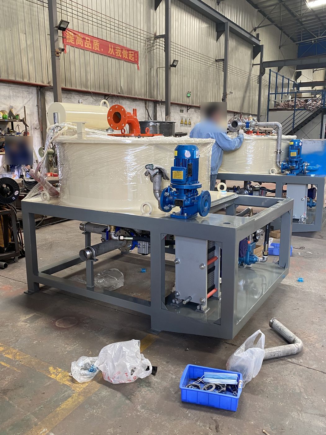 Two slurry separators on grey steel frames with blue pumps and pipework, being assembled in the PTMS workshop